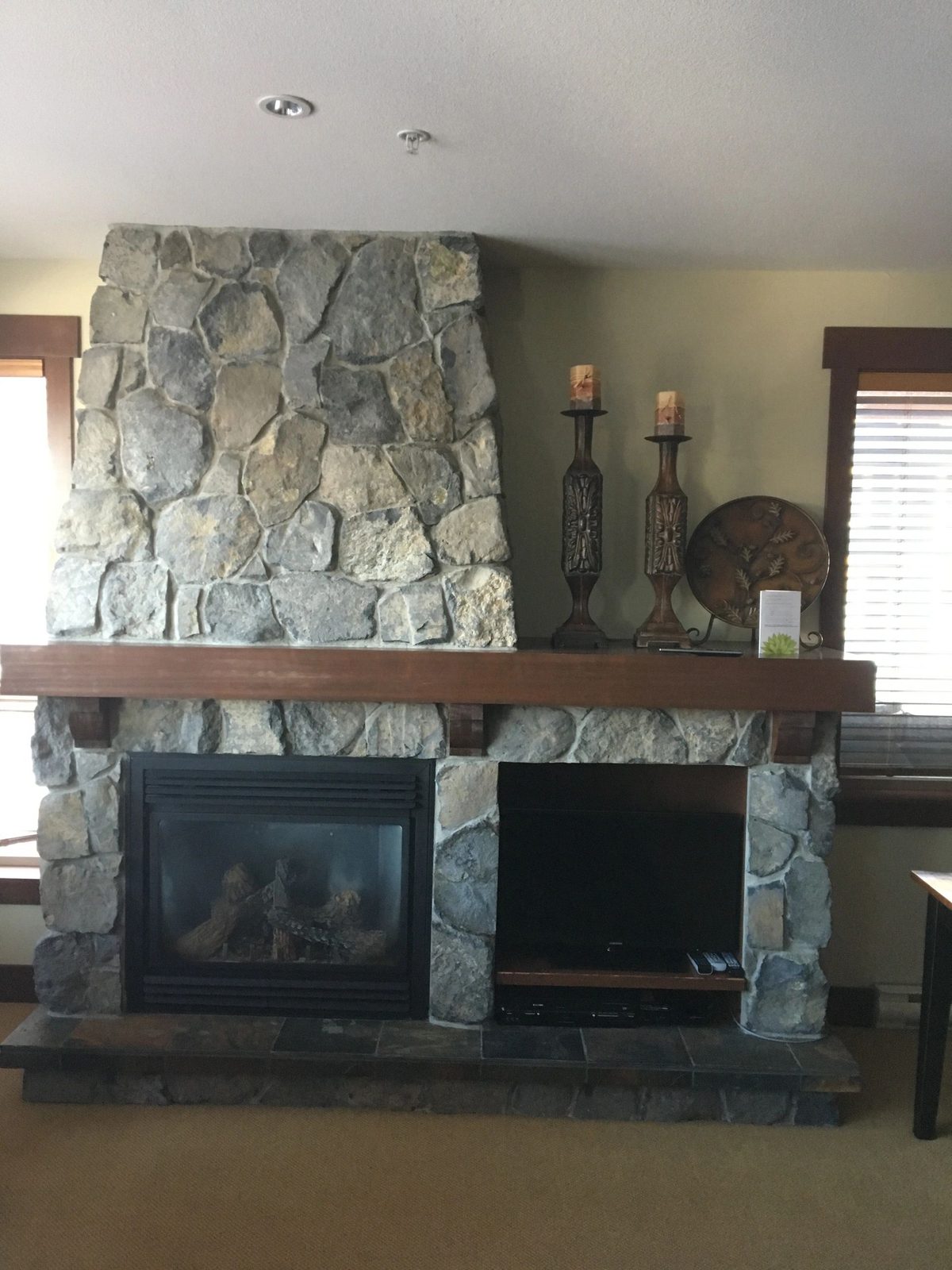 River rock fireplace with a mounted TV and timber mantle