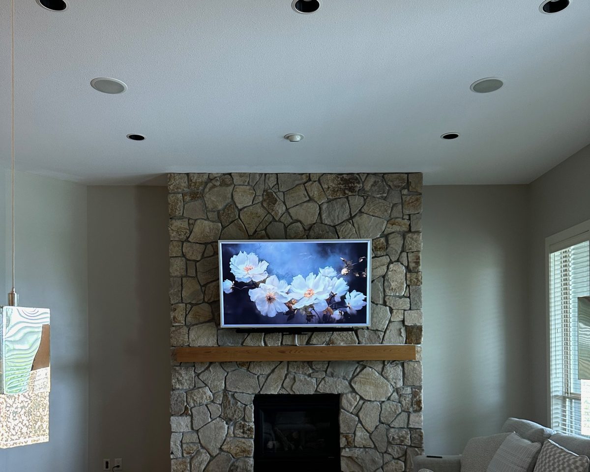 Frame TV on a fieldstone chimney with a timber mantel in a lake view living room
